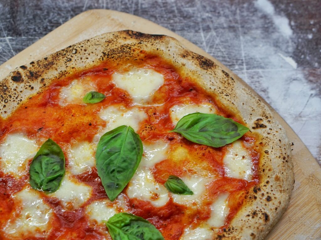 Pizza neapolitańska z bazylią na wierzchu leży na drewnianej desce.