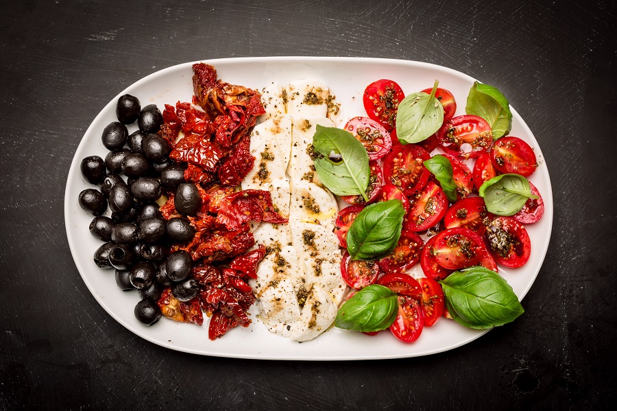 Półmisek z caprese, oliwkami i suszonymi pomidorami, posypane świeżą bazylią.