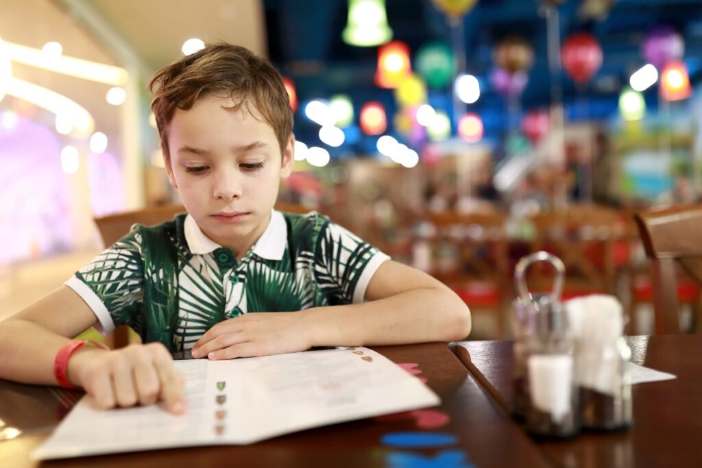 Chłopiec przy stole czyta menu, śledząc palcem tekst 