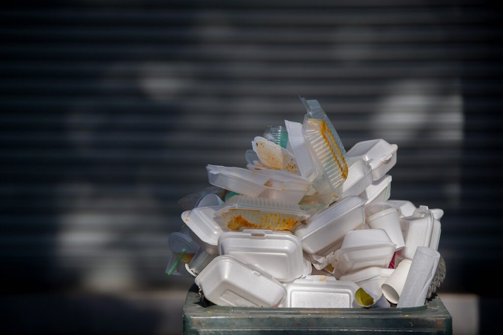 Opakowania jednorazowe po jedzeniu wystają z kubła na śmieci. 